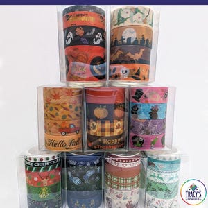 May include: A collection of holiday washi tape sets stacked in clear plastic boxes. The tapes feature seasonal designs including Halloween ghosts, pumpkins, Thanksgiving motifs, autumn leaves, Christmas reindeer, snowflakes, and festive patterns.