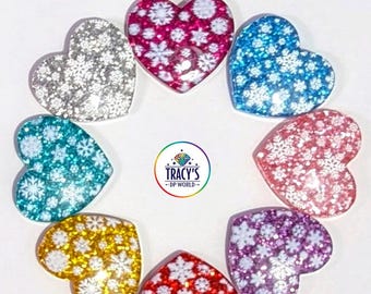 May include: A collection of heart-shaped cover minders in various colors, including silver, pink, blue, teal, gold, red, and purple. Each heart features a snowflake design. The text "WINTER HEARTS COVER MINDERS" is at the top.