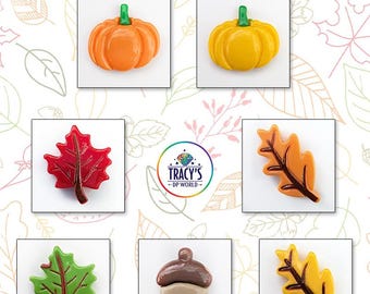 May include: A collection of seven autumn-themed cover minders featuring pumpkins, leaves, and an acorn in orange, yellow, red, green, and brown. The text reads AUTUMN COVER MINDERS and AVAILABLE IN 7 STYLES, with a central logo for TRACY'S DP WORLD.