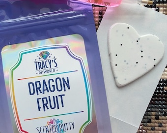 May include: A purple pouch of Dragon Fruit Scented Putty with a label that reads "Dragon Fruit Scented Putty" and a heart-shaped putty with black dots. The image also includes a pink tool and a logo that says "Tracy's DP World."