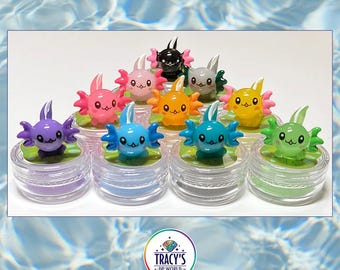 May include: A collection of colorful axolotl figurines atop small, clear containers. The axolotls are in various colors, including pink, blue, and yellow. The text "AXOLOTL LILYPADS" is at the top. The text "WET THE SPONGE - WORKS WITH WAX OR PUTTY" and "KEEPS ABS FROM STICKING" are at the bottom.