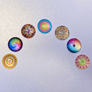 May include: Seven colorful round cover minders with different rainbow-inspired designs. The cover minders are arranged in a semi-circle on a white background.