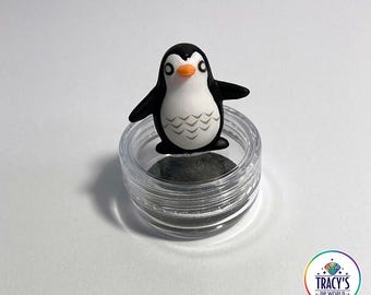 May include: A small, black and white penguin figurine with an orange beak sits atop a clear, round container. The text "LILYPADS - PENGUIN" is at the top. The text "WET THE SPONGE - WORKS WITH WAX OR PUTTY" and "KEEPS ABS FROM STICKING" are at the bottom.