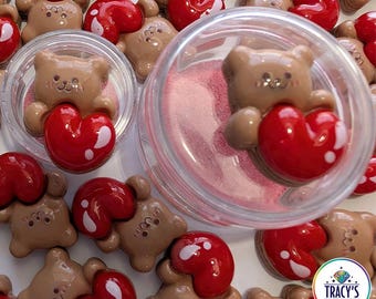 May include: The image showcases brown bear-shaped charms holding red heart-shaped accents. The text "HEART BEARS" is at the top, with "AVAILABLE AS A COVER MINDER OR AS A REGULAR OR LARGE LILYPAD" at the bottom. Some charms are in clear containers.