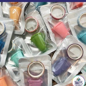 May include: Set of three silicone finger protectors in various colors, each packaged with a roll of patterned washi tape.  The text "SET OF 3 - RANDOM COLOR - INCLUDES A ROLL OF WASHI TAPE" is printed on the bottom of the image.