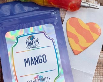 May include: A blue pouch labeled MANGO SCENTED PUTTY with a holographic sticker featuring the text TRACY'S DP WORLD. Beside it is a heart-shaped piece of orange and yellow putty and a multi-colored resin tool with a metal tip for diamond painting.