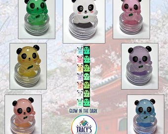 May include: A collection of panda-shaped accessories in various colors, each sitting in a small, clear container. The pandas have black and white faces and are shown in green, white, pink, yellow, purple, peach, and blue. The text "PANDA LILYPADS" and "GLOW IN THE DARK" are visible.