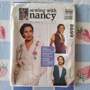 May include: A sewing pattern envelope with a white background and a colorful image of a woman wearing a white jacket with pink and blue embroidery. The text on the envelope reads "sewing with nancy" and "Patterns by Nancy Zieman for McCall's". The pattern number is 8699.