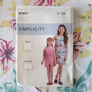 May include: A sewing pattern for children's clothing, Simplicity pattern number R10611, size UK 7-14, includes a dress, a top, and shorts.