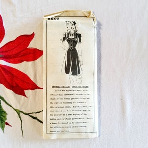 May include: A vintage sewing pattern for a dress for juniors. The pattern shows a black dress with a gathered dickey and ruffles on the sleeves. The text on the pattern reads "Demurely Detailed Dress for Juniors".