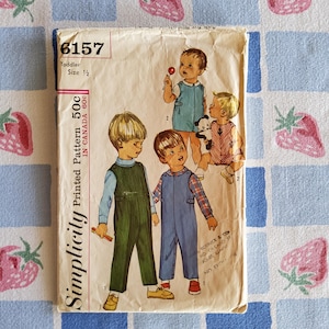 Pode incluir: Padrão impresso Simplicity vintage 6157 para tamanhos de criança 1/2. O padrão apresenta ilustrações de crianças em macacões e jardineiras. O padrão é impresso em papel envelhecido com o texto "Simplicity" e "50c in Canada 60c".