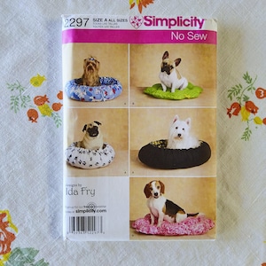 May include: A Simplicity sewing pattern for no-sew dog beds. The pattern features various dog breeds in different bed designs. The pattern cover is pink and white with the number 2297 and the Simplicity logo.