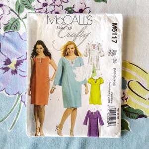 May include: A McCall's sewing pattern envelope featuring illustrations of dresses in orange, light blue, white, yellow, and purple. The envelope includes the text "McCall's Make It Crafty" and size information.