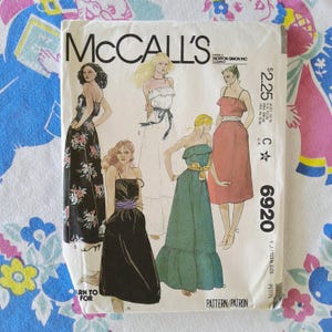 May include: A McCall's 6920 sewing pattern envelope featuring illustrations of five different dress styles. The designs include a black floral maxi dress, a white strapless dress, a black midi dress, a teal ruffled maxi dress, and a pink midi dress.