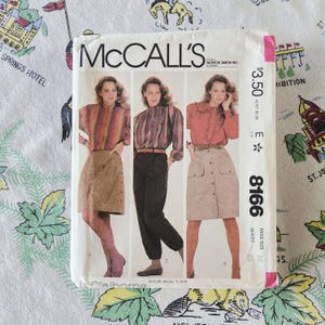 May include: McCall's sewing pattern 8166 featuring three garment variations: a striped blouse with a tan skirt, a plaid blouse with dark trousers, and a solid rust-colored blouse with a tan button-front skirt. The envelope displays the price $3.50.