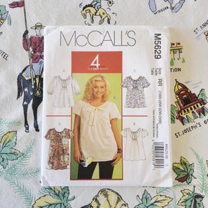 May include: A white McCall's M5629 sewing pattern envelope featuring four variations of a blouse with gathered necklines and short sleeves. The front displays a central photograph of a person wearing a cream-colored blouse with a tie-front detail.