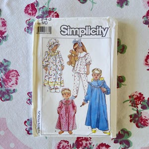 以下が含まれることがあります： 子供用寝間着のヴィンテージSimplicityソーイングパターン。パターンには、ネグリジェ、パジャマ、ローブなど、さまざまなパジャマスタイルのイラストが掲載されています。パッケージはクリーム色で、Simplicityのロゴと製品の詳細が記載されています。