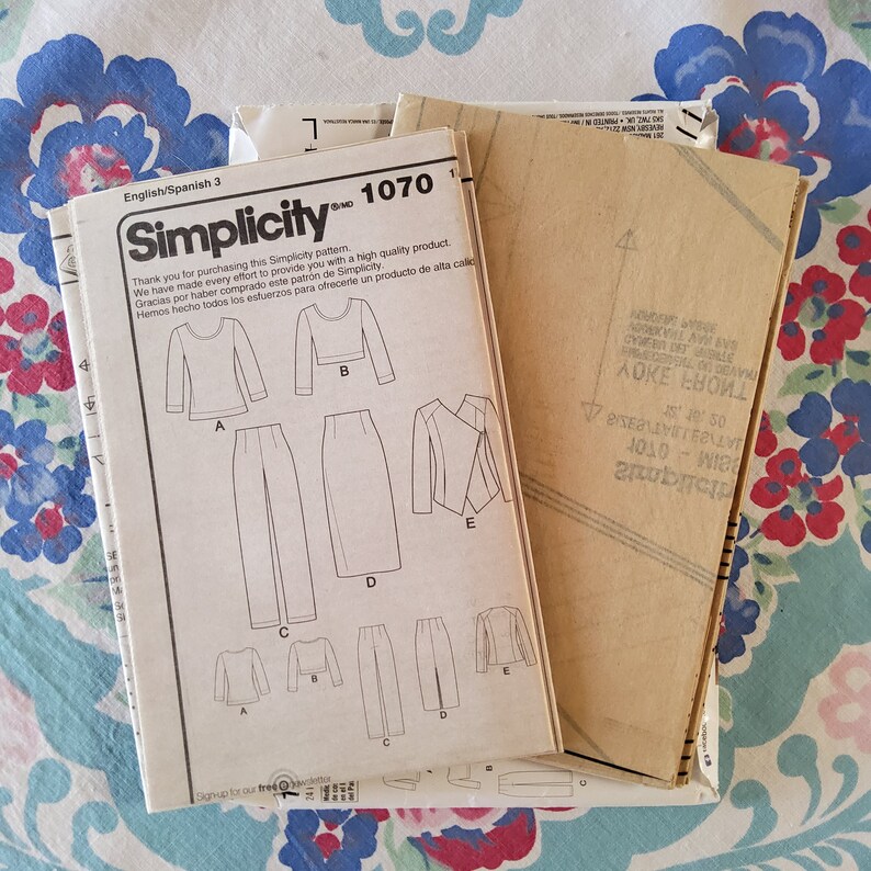 May include: A Simplicity sewing pattern for a women's clothing set. The pattern includes instructions for a long-sleeved top, trousers, and a skirt. The pattern number is 1070.