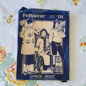 Op de afbeelding: Een vintage Folkwear naaipatroonpakket met illustraties van Chinese jassen. Het donkerblauwe pakket heeft de tekst "Folkwear" en "Chinese Jacket". De illustraties tonen vrouwen in traditionele Chinese kleding, met waaiers en gedetailleerde kledingstukken.