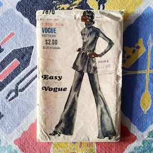 May include: Vintage Vogue sewing pattern packet. The packet features a fashion illustration of a woman in a flared jumpsuit. The text on the packet reads "Very Easy Very Vogue" and includes sizing information.
