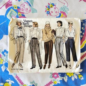 Puede incluir: Patrón de costura Vogue Basic Design vintage 1445. El patrón presenta ilustraciones de diseños de moda femenina, incluyendo pantalones, chaquetas y suéteres. La portada es blanca con texto e ilustraciones en negro y marrón.
