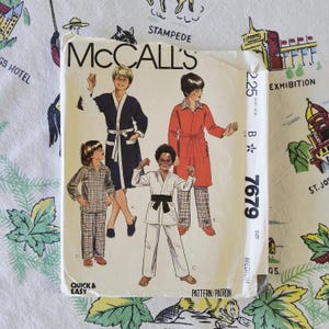 May include: A McCall's sewing pattern envelope 7679 for medium-sized loungewear and martial arts attire. The cover features illustrations of four individuals wearing a dark blue robe, a red robe, plaid pajamas, and a white karate uniform with a black belt.