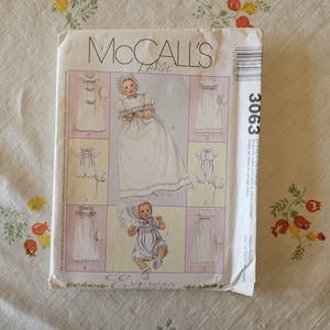 May include: A McCall's sewing pattern envelope, number 3063, size Large. The front features illustrations of infants wearing various styles of long gowns, rompers, and bonnets. The text includes the brand name, pattern number, and size label.
