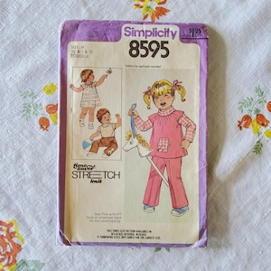 May include: Vintage Simplicity pattern 8595 for toddler clothing. The pattern envelope features illustrations of children's outfits, including a pink outfit with an elephant applique and a striped shirt with brown pants. The envelope is purple and white.