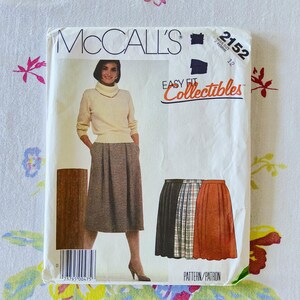 May include: McCall's sewing pattern 2152 for a miss size 12. The envelope features a photograph of a person wearing a cream-colored turtleneck sweater and a pleated, plaid midi skirt. Additional illustrations show three skirt variations in solid black, plaid, and solid rust orange.