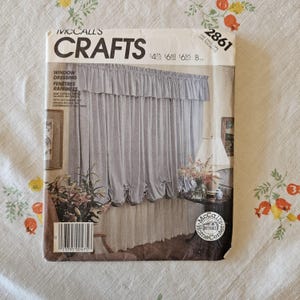 May include: A McCall's Crafts sewing pattern envelope 2861 for window dressing. The front features a photograph of light gray ruffled curtains, a table lamp, and a floral arrangement. The text includes the brand name, pattern number, and prices.