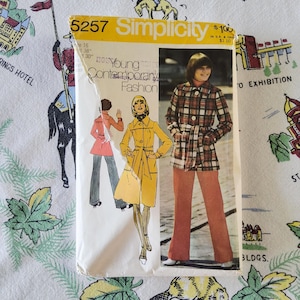 May include: A Simplicity 5257 sewing pattern envelope for Young Contemporary Fashion. The cover features illustrations of a yellow belted coat and a photograph of a person wearing a plaid jacket with a belt and solid-colored trousers.