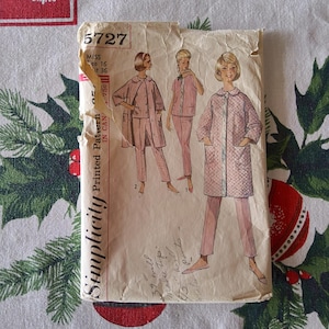 May include: Vintage Simplicity sewing pattern packet. The packet features illustrations of women's sleepwear in pink. The packet is labeled with the number 5727 and includes measurements. The background is a festive Christmas-themed fabric.