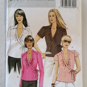 May include: A sewing pattern for a wrap top with a ruffled neckline. The pattern includes four different styles: a white top with long sleeves, a brown top with short sleeves, a pink top with long sleeves, and a red and white gingham top with short sleeves. The pattern is for sizes 8-10-12-14. The pattern number is B5328/BB.