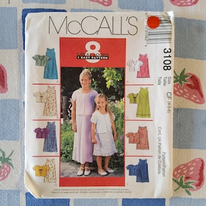 May include: McCall's sewing pattern number 3108 for girls' dresses. The pattern includes eight different styles of dresses, including a pink dress with white polka dots, a yellow dress with a bow, and a lavender dress with a white cardigan. The pattern is for sizes 4-5-6.