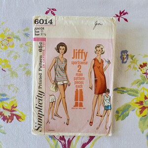 May include: A vintage Simplicity 6014 sewing pattern envelope for junior size 11, bust 31.5 inches. The cream and pink package features illustrations of sportswear, including a striped sleeveless top, shorts, and a solid orange dress with side buttons.