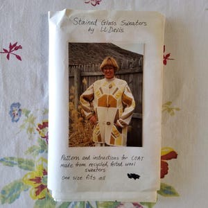 May include: A pattern and instructions for a coat made from recycled, felted wool sweaters. The pattern is called "Stained Glass Sweaters" by LL Davis. The pattern includes a photo of a woman wearing the coat, which is white with brown and yellow geometric shapes.