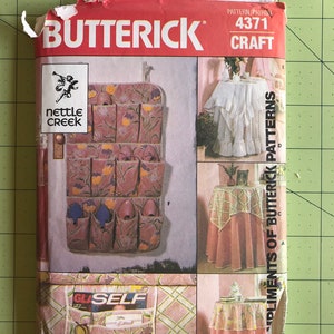 May include: A vintage sewing pattern from Butterick, pattern number 4371, for a craft project. The pattern includes instructions for making a wall organizer with pockets, a table runner, and a tablecloth. The pattern is titled "Compliments of Butterick Patterns".