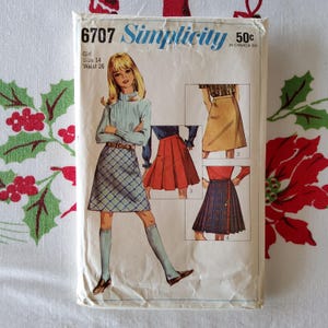 Könnte beinhalten: Vintage Simplicity Schnittmuster Nummer 6707 für einen Mädchenrock. Das Schnittmuster enthält vier verschiedene Rockstile: einen karierten Rock, einen roten Faltenrock, einen braunen Rock und einen karierten Kiltrock. Das Schnittmuster ist für die Größen 14 mit einem Taillenumfang von 66 cm.