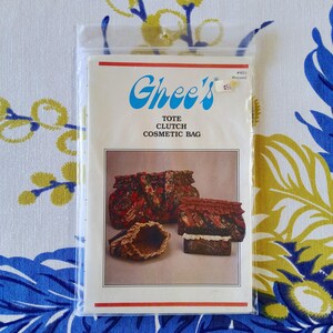May include: A clear plastic bag containing a sewing pattern for a tote, clutch, and cosmetic bag. The pattern is labeled "Ghee's" with a red and white border. The pattern shows images of the finished bags in floral fabric.