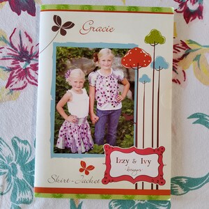 May include: A pink and purple skirt and jacket sewing pattern with a photo of two girls wearing the pattern. The pattern is called "Gracie" and is from "Izzy & Ivy Designs".