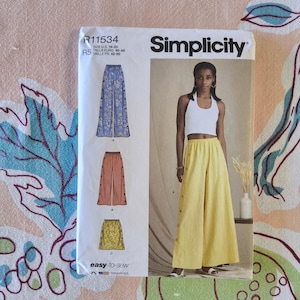 May include: Simplicity sewing pattern R11534 featuring wide-leg pants. The pattern includes size options from US 14-22. The image shows a model wearing yellow wide-leg pants with button details. The pattern is easy-to-sew.