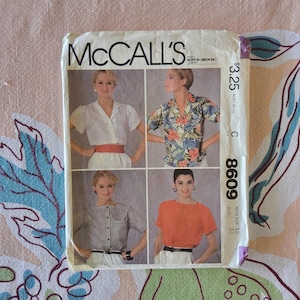 Può includere: Cartamodello vintage McCall's con quattro modelli di camicette. La busta del modello mostra le immagini delle camicette, con il logo McCall's in alto. Il numero del modello è 8609 e la misura del busto è 86 cm.