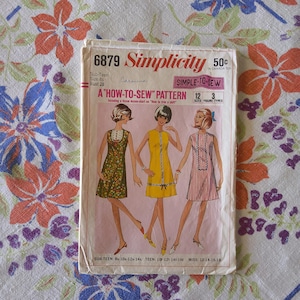 Puede incluir: Patrón de costura Simplicity vintage, número 6879, con un patrón "Cómo coser" para vestidos. La portada muestra tres diseños de vestidos en varios colores y estampados. El patrón incluye tallas para adolescentes, jóvenes y mujeres.