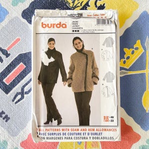 May include: A Burda jacket sewing pattern package featuring images of two women wearing jackets. The package includes the words "JACKE, VESTE, JACKET, CHAQUETA" and "ALL PATTERNS WITH SEAM AND HEM ALLOWANCES". The package is white with a colorful background.