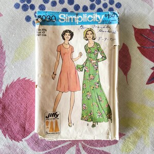 May include: Vintage Simplicity sewing pattern featuring illustrations of two dresses. The pattern includes a short peach dress and a long green floral dress. The pattern is labeled "7030" and includes the text "Jiffy".
