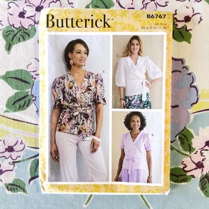May include: Butterick sewing pattern B6767 featuring three wrap top designs. The pattern includes a floral print top, a white top with ruffled sleeves, and a lavender top. The pattern size is A5 (6-8-10-12-14).