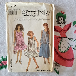 Puede incluir: Patrón de costura Simplicity número 8701 para las tallas 10, 12 y 14. El patrón es para un vestido con una falda fruncida y un corpiño ajustado. El patrón incluye tres estilos diferentes de vestidos: un vestido de estampado floral rosa, un vestido blanco con rayas blancas y negras y un vestido azul con ribete de encaje blanco. El patrón se titula "Great Expectations" y "Attendant le Grand Evénement".