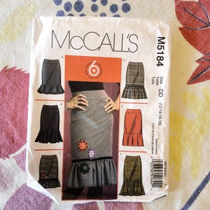 May include: A McCall's sewing pattern envelope, M5184, featuring illustrations of six skirt designs. The envelope is white with black text and images, including a central image of a skirt with floral embellishments. Size DD (12-14-16-18).