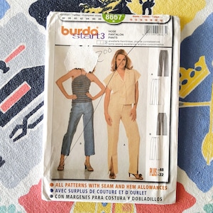Peut inclure: Un patron de couture vintage Burda Start 3 pour pantalons, avec des illustrations de différents styles de pantalons. Le patron comprend les tailles 10-22 et les tailles européennes 36-48. La couverture montre une femme en haut rayé et jean, et une autre en tailleur pantalon beige.