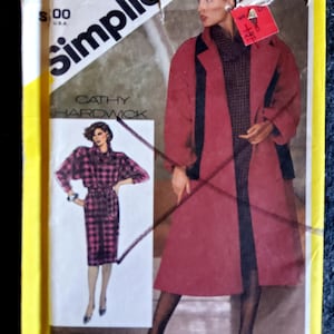 Può includere: Un cartamodello Simplicity con un cappotto rosso con bordatura nera e un abito a quadri. Il cartamodello è di Cathy Hardwick ed è taglia 10.